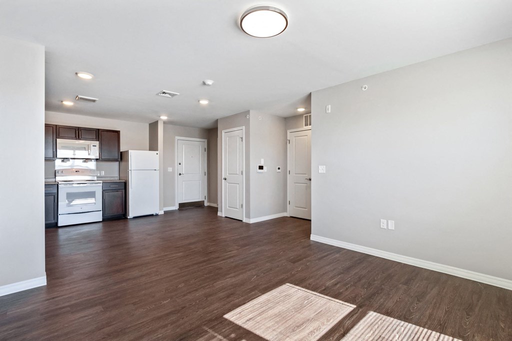 an empty living room and kitchen with wood flooring and white walls