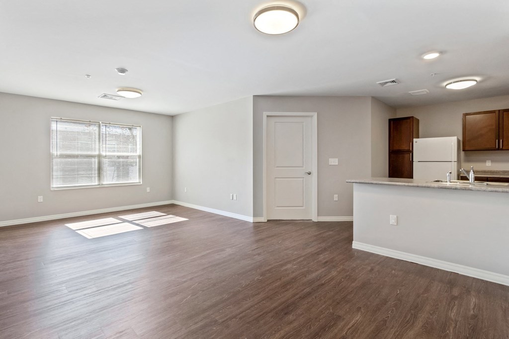 an empty living room with a kitchen and a white door