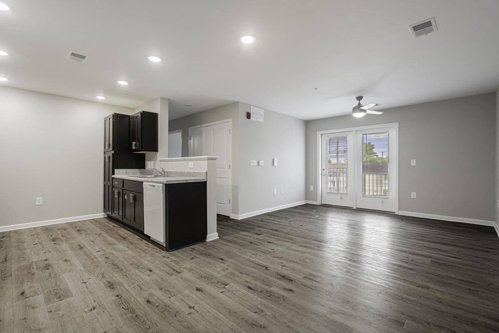 an empty living room with a kitchen and a door to a balcony