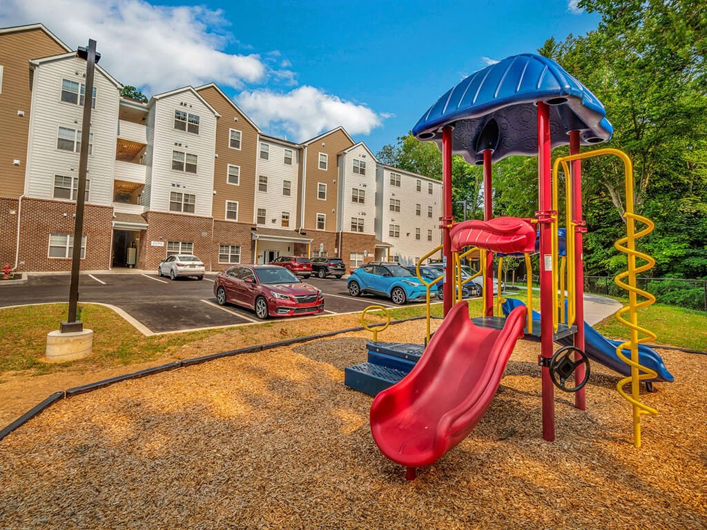 a playground with a red slide and a blue umbrella in front of an apartment building