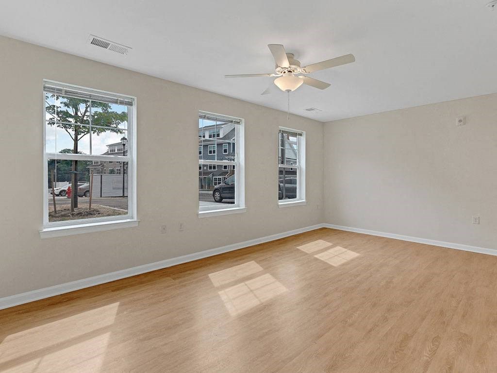 an empty living room with a ceiling fan and three windows
