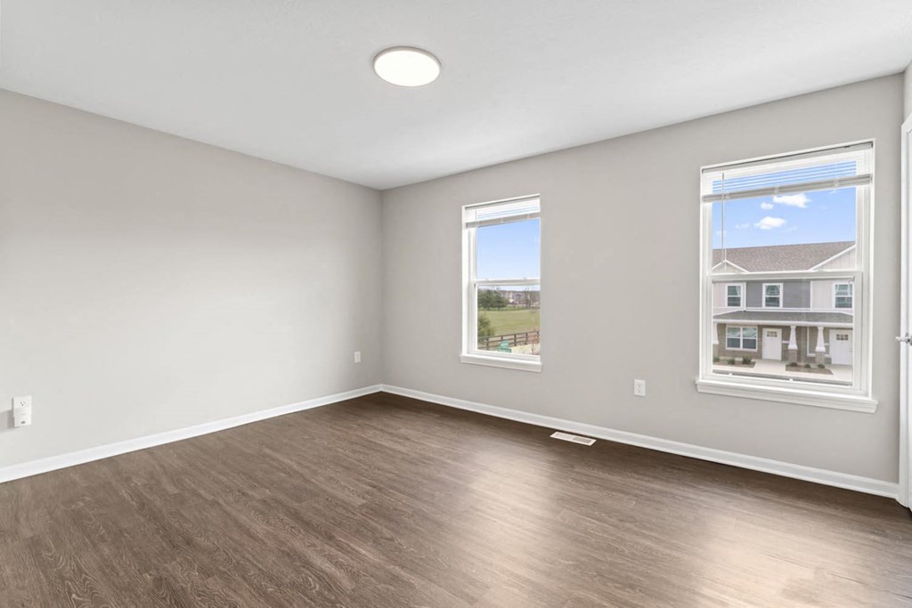 an empty living room with wood flooring and two windows