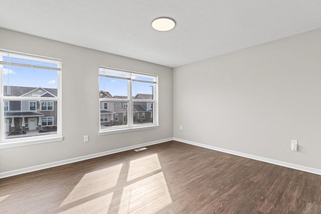 an empty living room with a hardwood floor and three windows