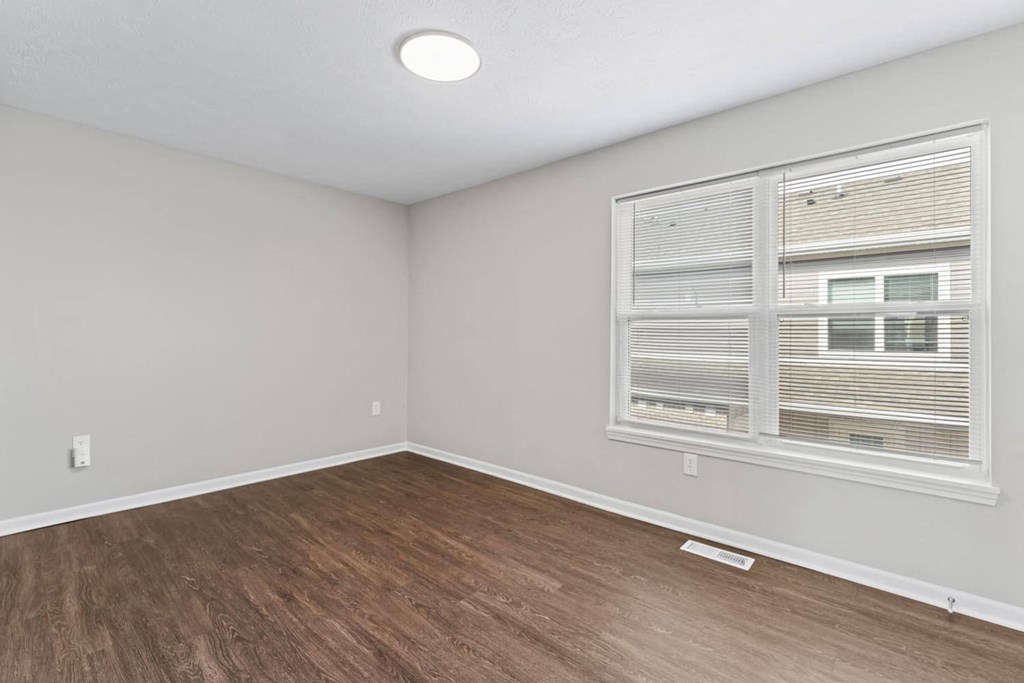 an empty living room with a large window and wooden floors