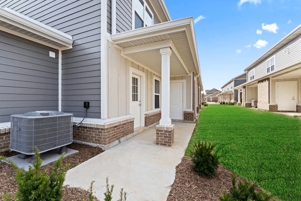 a walkway leading to a house with a yard and a cooling unit