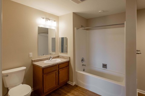 A bathroom with a white toilet, a wooden vanity with a sink, and a white bathtub.