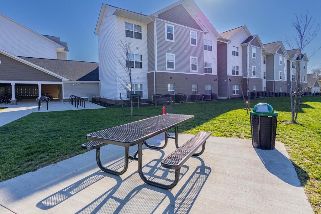 A park with a picnic table and bench in front of apartment buildings.