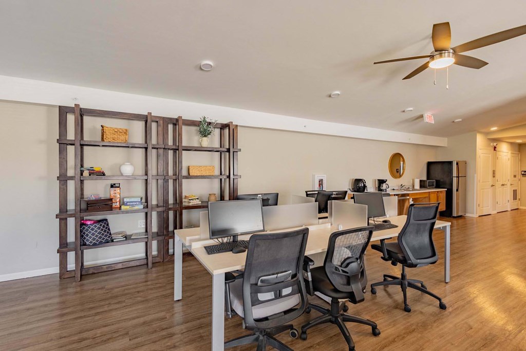 A room with a desk, chairs, and a ceiling fan.