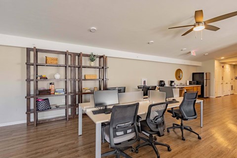 A room with a desk, chairs, and a ceiling fan.