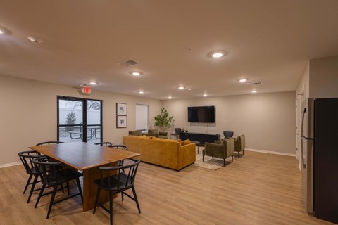 A room with a long table and chairs, a couch, a television, and a plant.