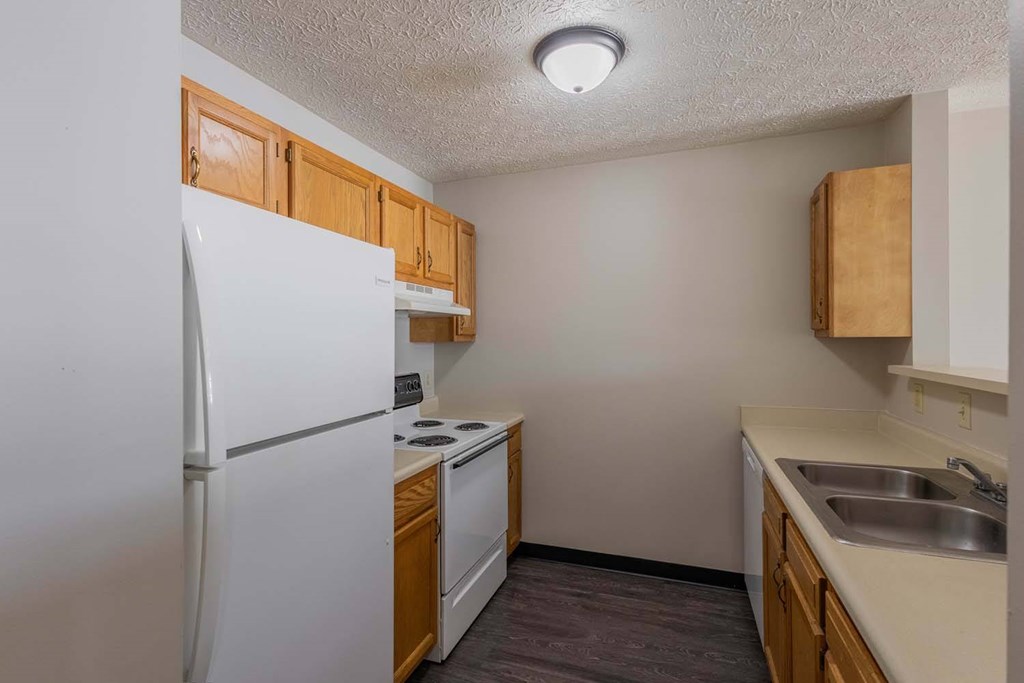 A kitchen with a white refrigerator, wooden cabinets, and a sink.
