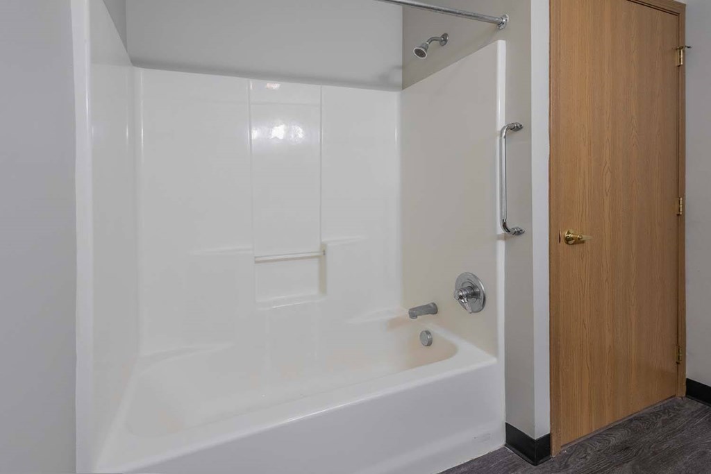 A white bathtub with a shower head and a wooden door.