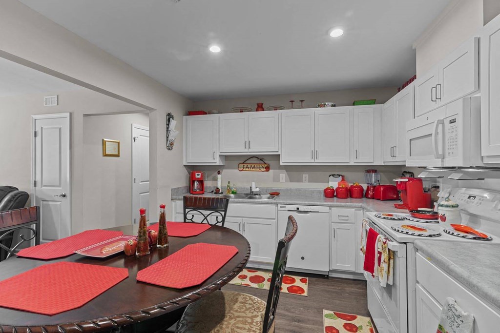a kitchen with white cabinets and a table with red chairs