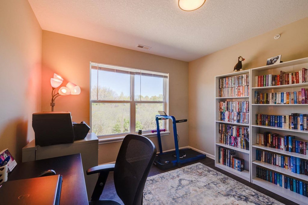a home office with a bookshelf and treadmill