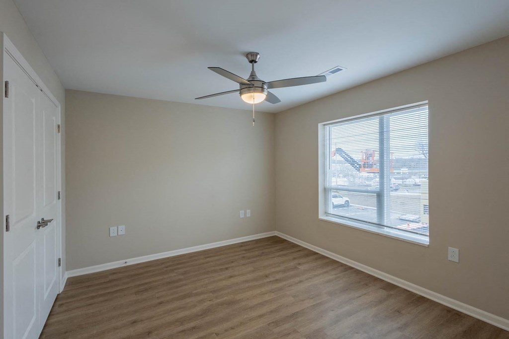 A room with a ceiling fan and a window overlooking a parking lot.