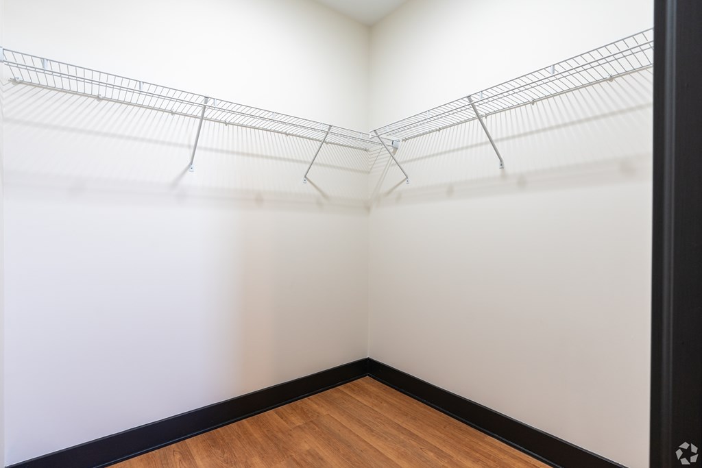 A white wire shelf in a corner of a room with wood flooring.