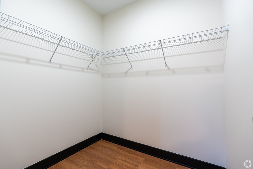 A room with a white wall and a wooden floor with a metal shelf on the wall.