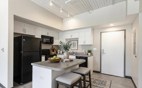 A kitchen with a black refrigerator, white cabinets, and a marble island.