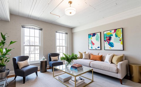 A living room with a white couch, two chairs, a coffee table, and two paintings on the wall.