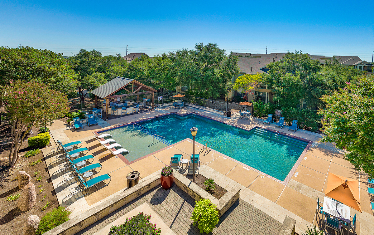A large outdoor swimming pool surrounded by lounge chairs and trees.