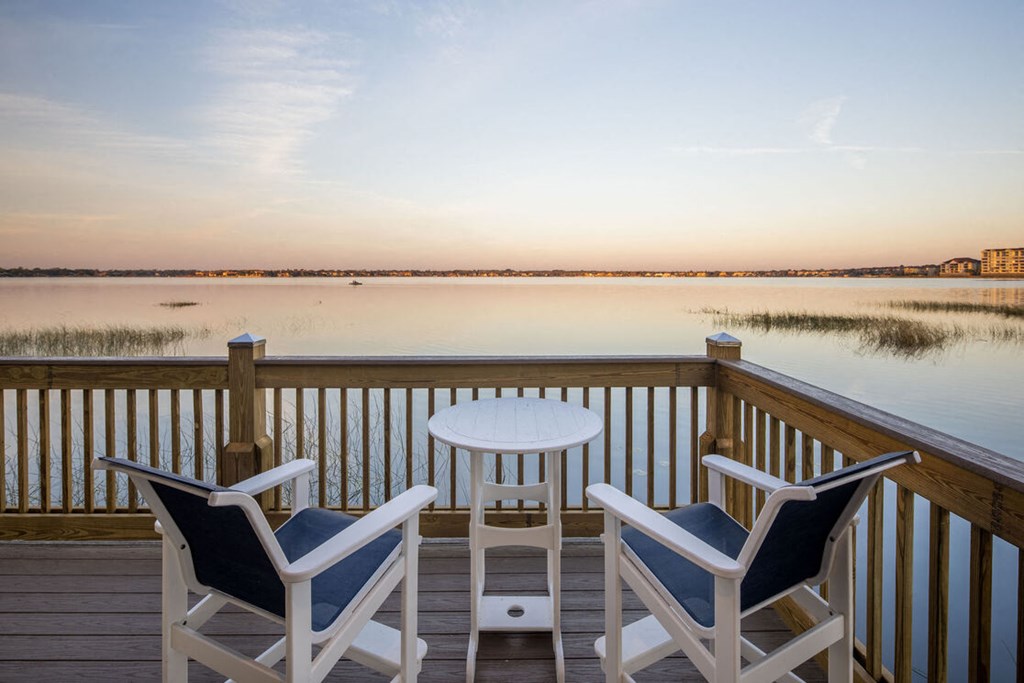 a patio with two chairs and a table on a deck overlooking a lake
