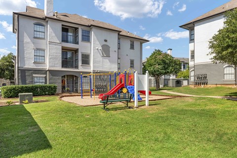 A playground with a slide and a bench in front of a building.