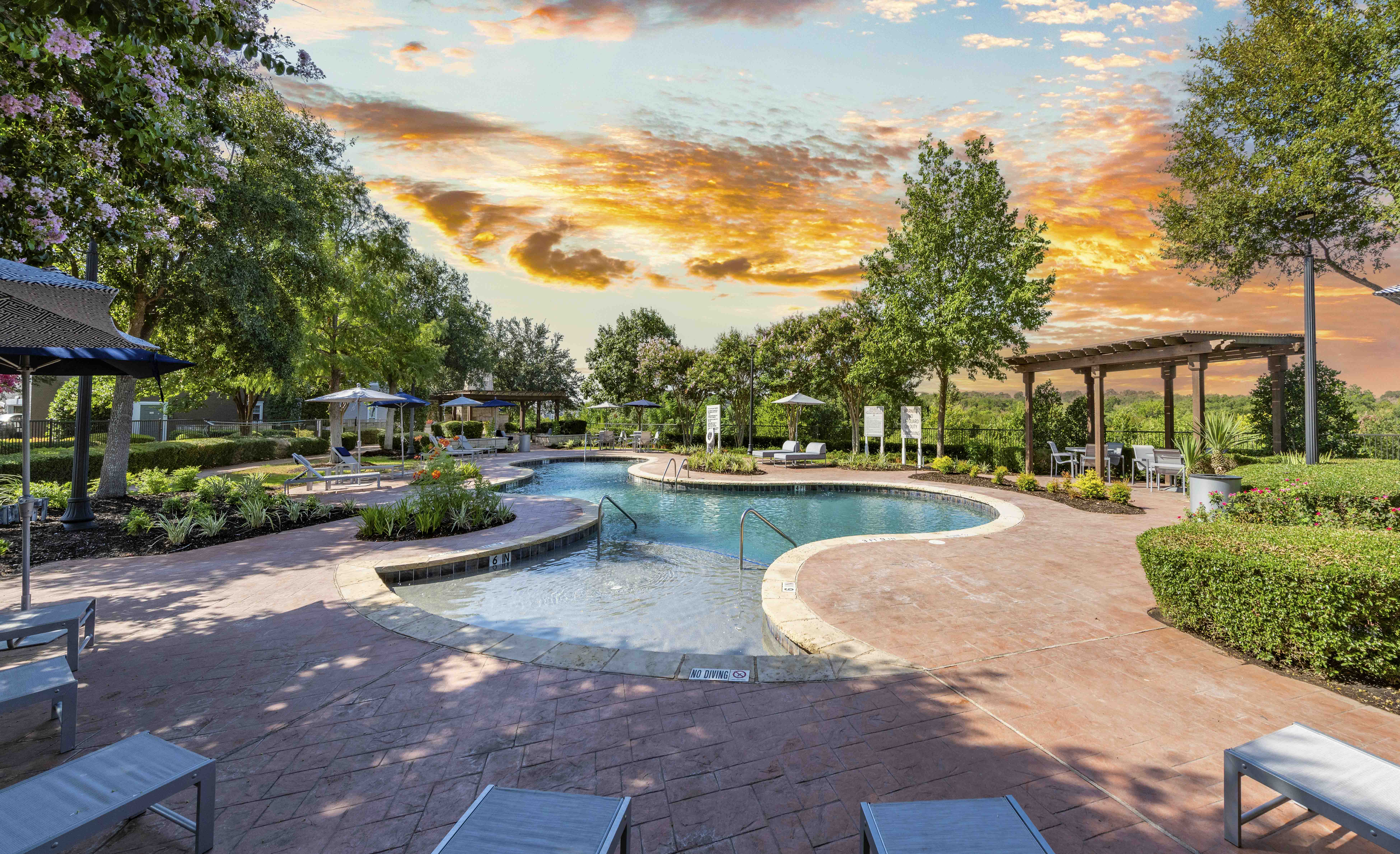 A sunset view of a pool area with a hot tub and seating area.