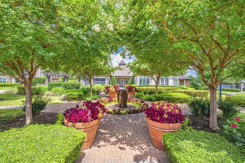 A garden with a circular brick pathway and two large pots of flowers in the middle.