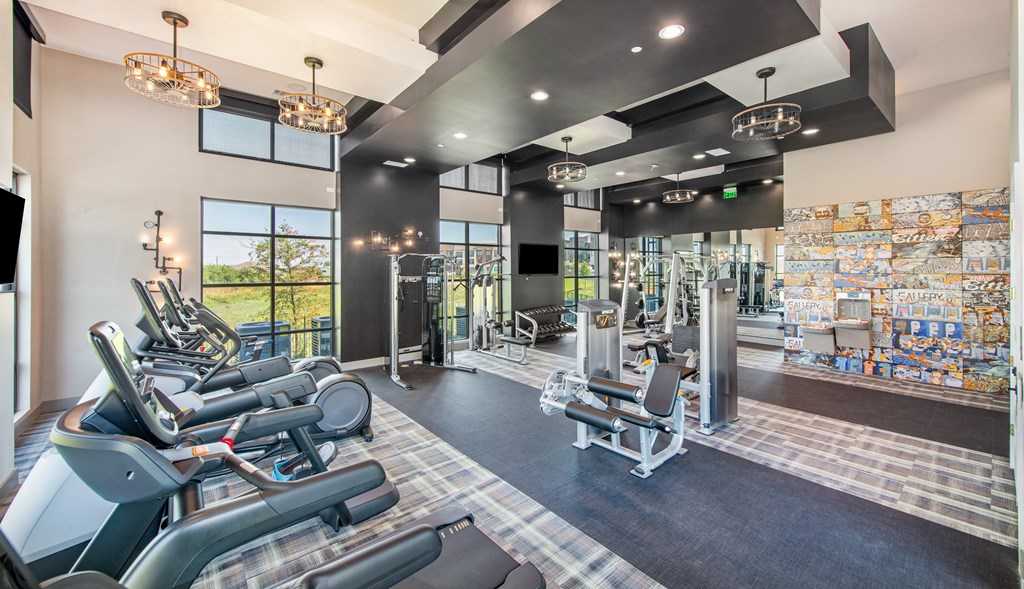 a gym with weights and cardio machines and a glass walled area with windows