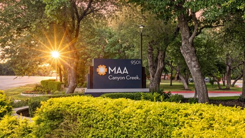 The image shows a sign for MA Canyon Creek with a sunset in the background.