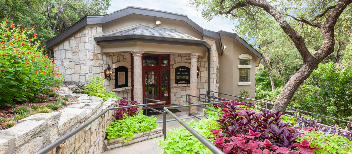 A small house with a red door is surrounded by greenery.