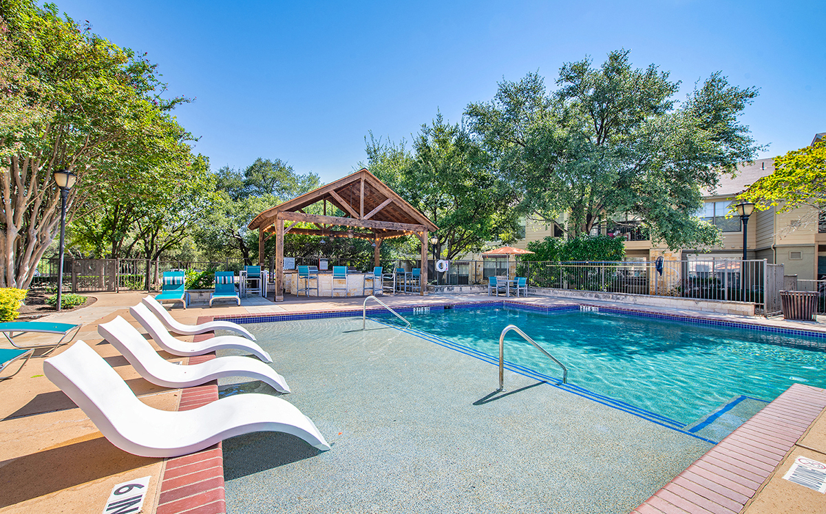 A pool with a white lounge chair and a gazebo in the background.