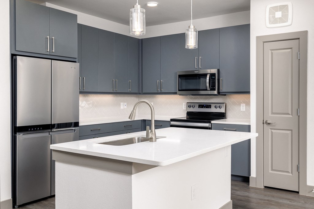an empty kitchen with a white counter top and stainless steel appliances