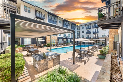 A sunset view of a pool area with lounge chairs and umbrellas.