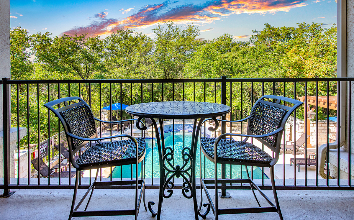 A table with two chairs is on a balcony overlooking a pool.