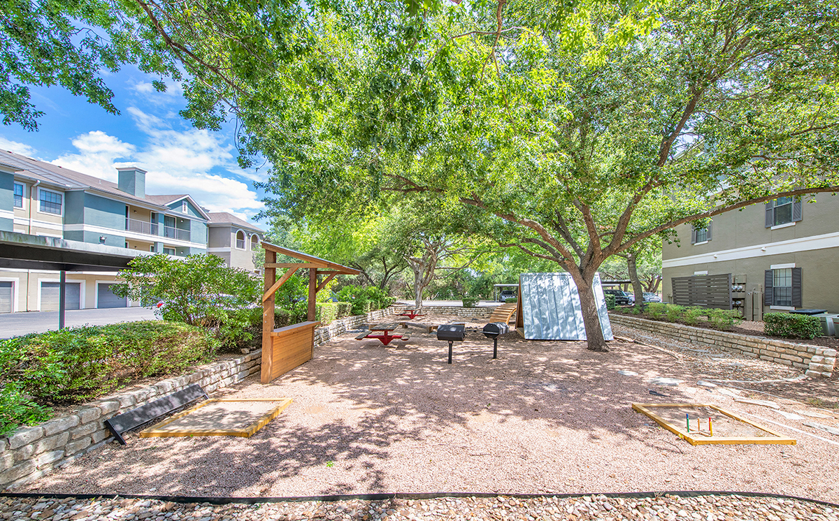 A tree in a yard with a swing set.