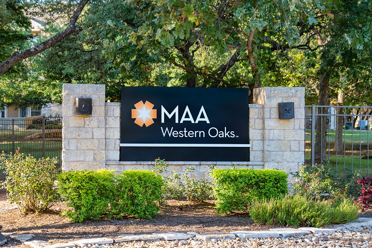 A sign for MAA Western Oaks is displayed in front of a fence and greenery.