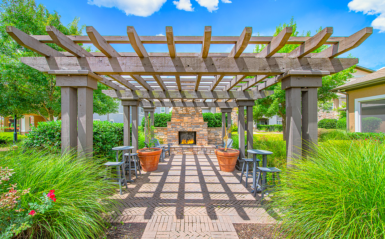A wooden pergola with a brick pathway leads to a fireplace.