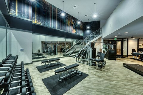 a gym with treadmills and chairs and a glass staircase