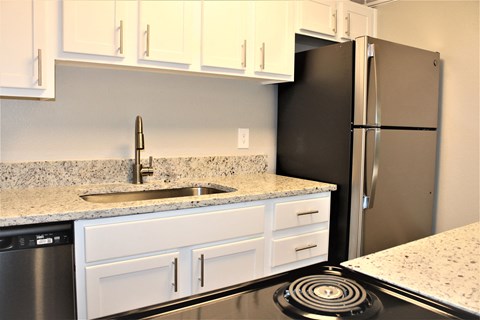 A kitchen with a black refrigerator and white cabinets.