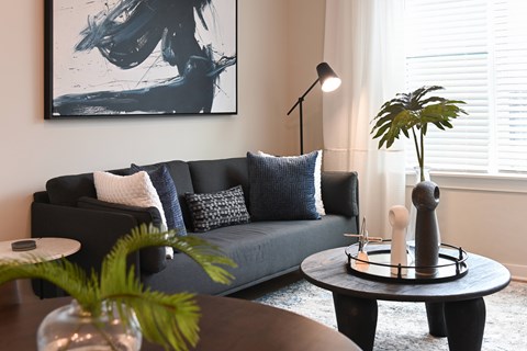 A living room with a grey couch, a black coffee table, and a large abstract painting on the wall.