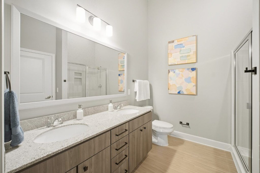 A bathroom with a sink, mirror, toilet and a shower.