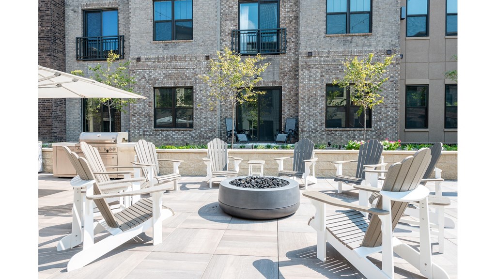 A patio with white chairs and a fire pit.