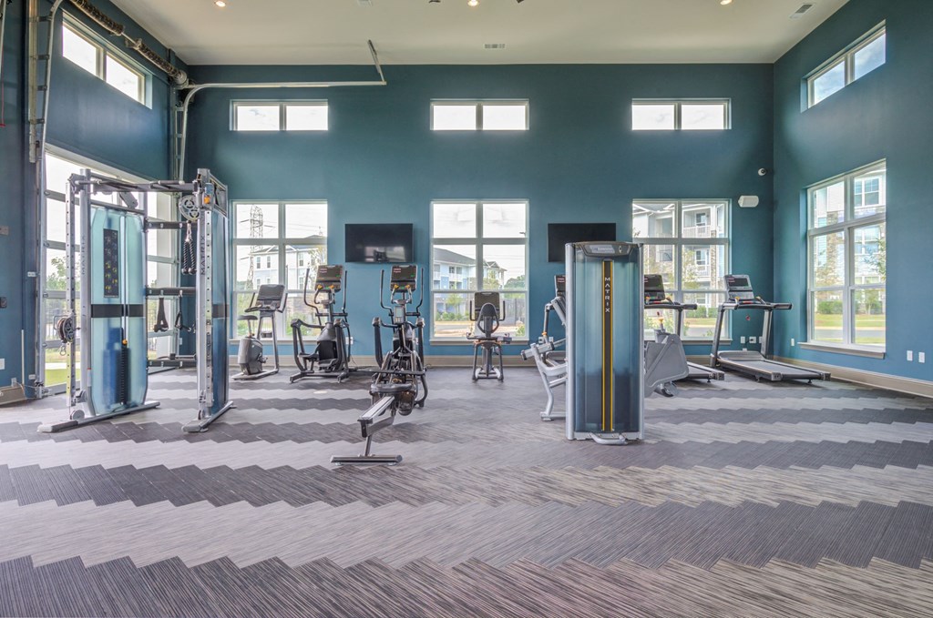 Gym inside with very tall ceilings, treadmills, bikes, machine weight lifting, eliptical machines and mix and match gym flooring.