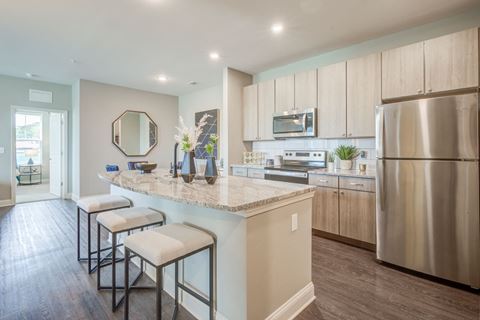one bedroom kitchen with gooseneck black faucet on the island,  woodgrain light cabinets, stainless steel appliances, granite countertops, kitchen table with blue leather chairs, 6-panel white doors, woodlike plank flooring, and laundry room off the kitchen