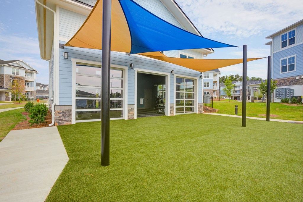 plush green grass yoga lawn outside the gym with rolling garage doors open to machines and free weights on the inside.