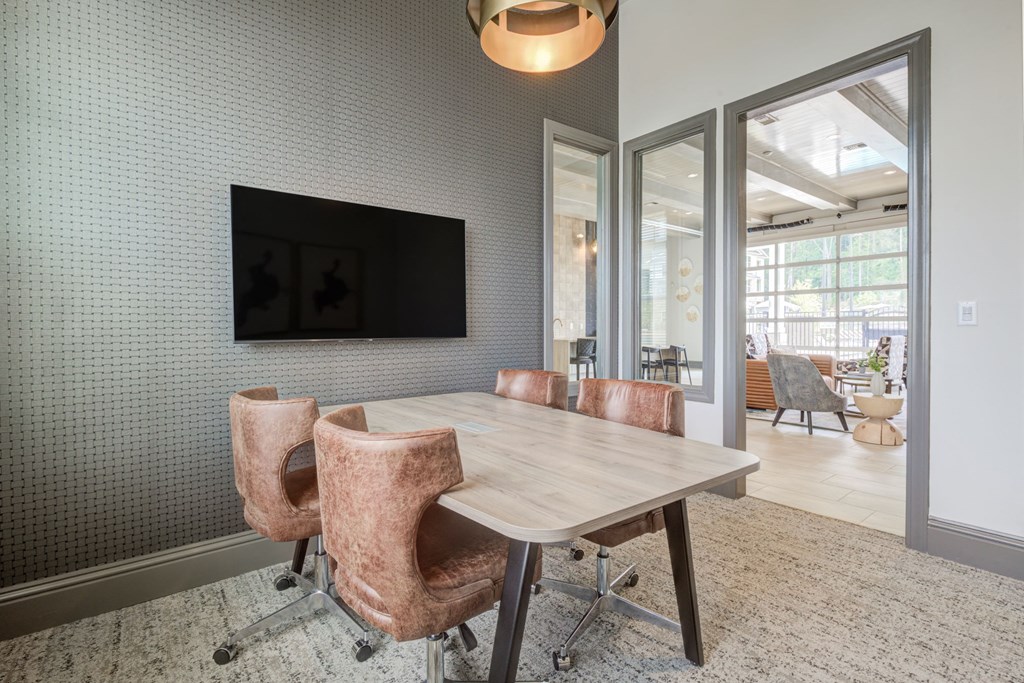 leasing office conference room with TV mounted on a wall with unique grey wall finish pattern.  Table has four leather executive chairs on carpet.
