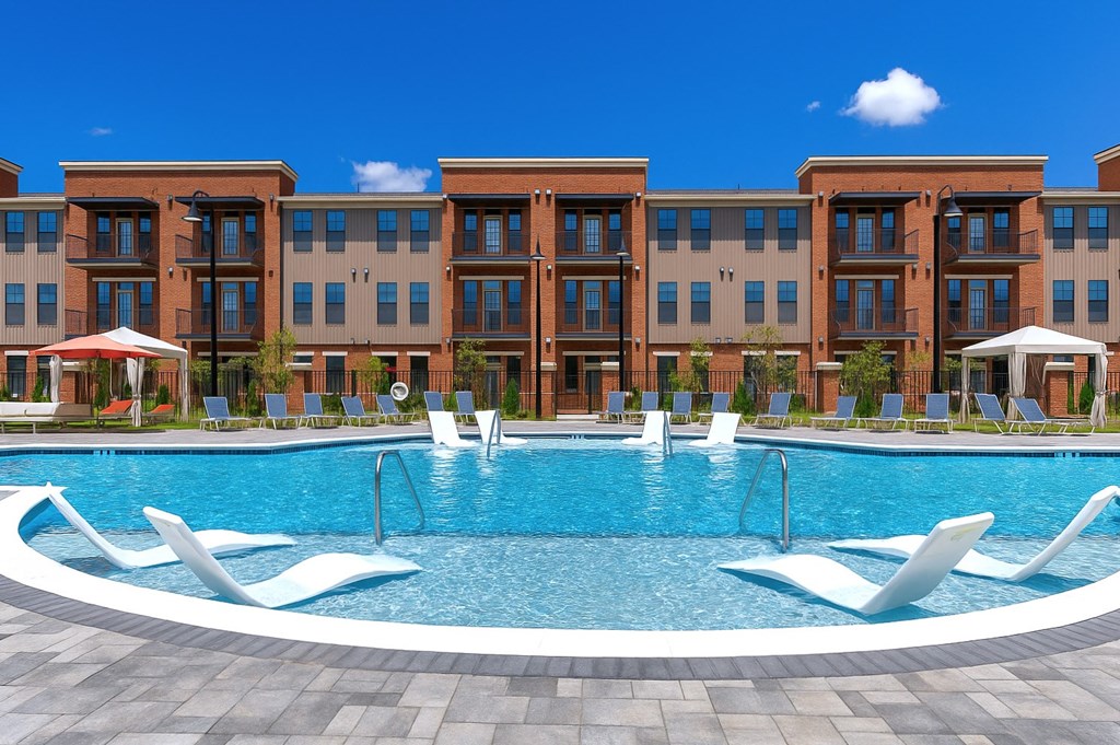 A large swimming pool in front of a building with lounge chairs around it.