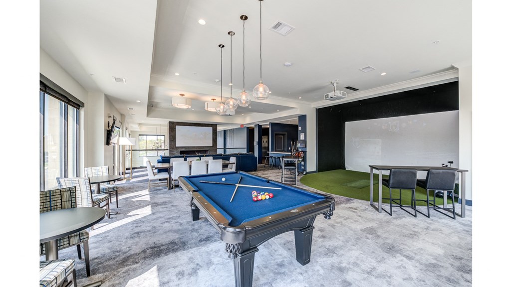 A pool table is in the middle of a room with a green rug and a dining table.