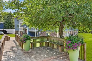 A wooden deck with a bench and two large pots of flowers.